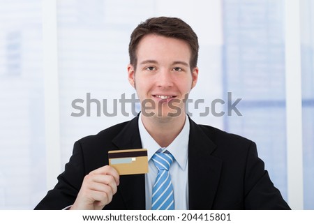 Portrait of confident young businessman holding credit card in office