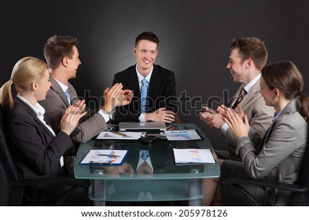 Young business people applauding for male colleague after presentation against black background