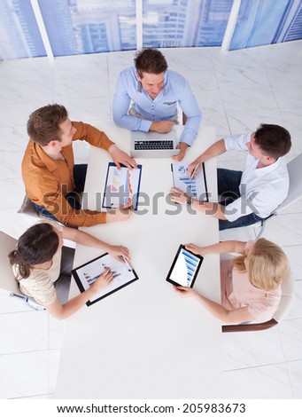 High angle view of young business people discussing on graphs at table in office