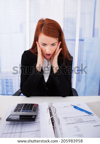 Shocked young businesswoman looking at tax papers at office desk