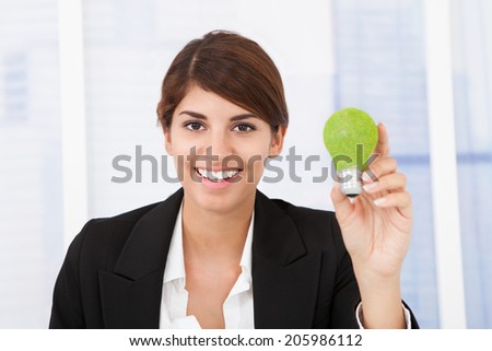 Portrait of happy businesswoman holding green light bulb in office