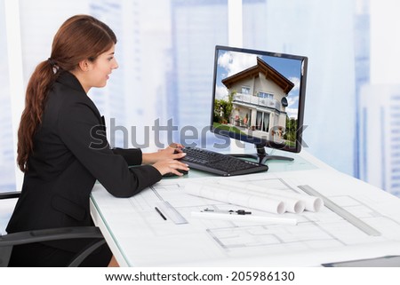 Side view of young female architect surfing house on computer at desk in office