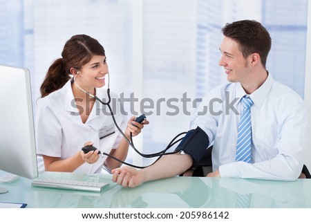 Young female doctor checking blood pressure of businessman in clinic