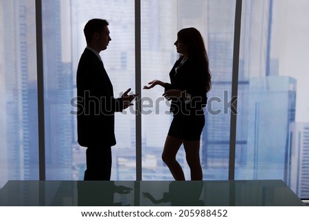 Side view of young businessman and businesswoman discussing by office window