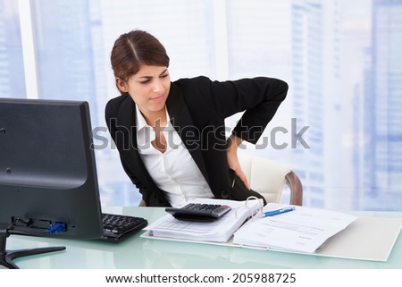 Tired young businesswoman suffering from backache sitting at computer desk in office