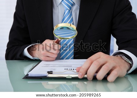 Midsection of young businessman examining invoice through magnifying glass at office desk