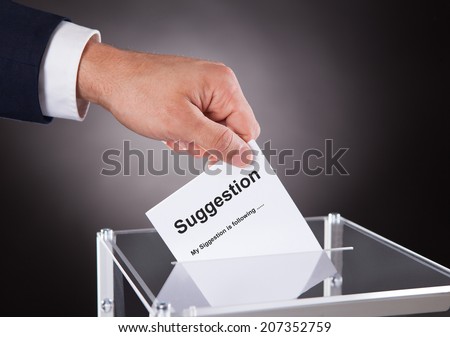 Cropped image of businessman placing suggestion slip into box over black background