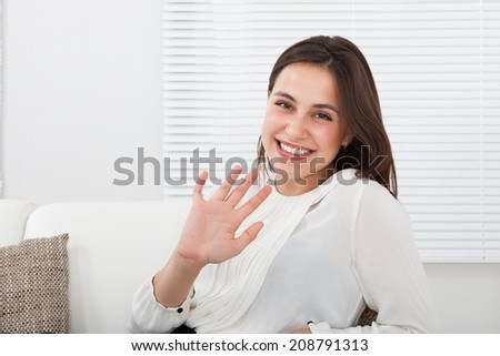 Portrait of happy businesswoman waving hand while relaxing on sofa at home