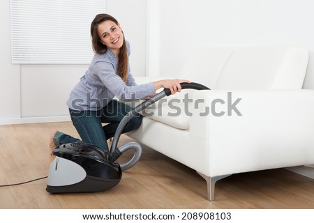 Full length side view of young woman vacuuming sofa at home
