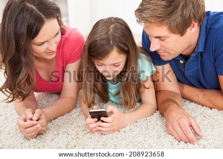 Parents looking at daughter using smart phone while lying on rug