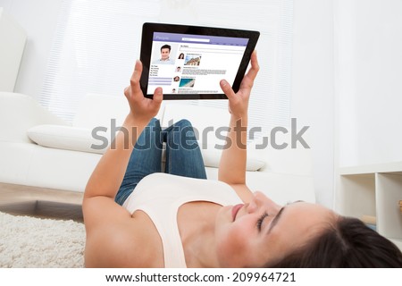 Young woman using digital tablet to chat on social site while relaxing at home