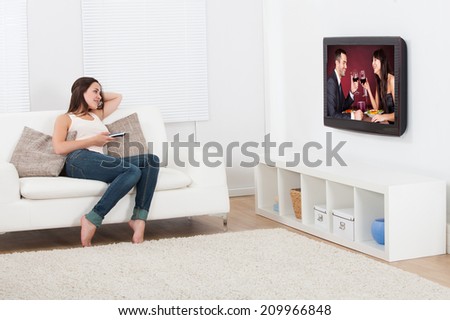 Full length of young woman watching television while lying on sofa at home