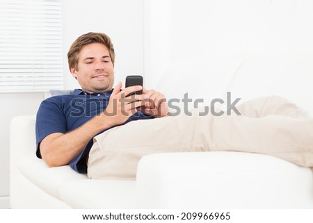 Relaxed man messaging on smart phone while lying on sofa at home