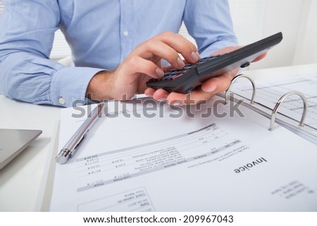 Cropped image of businessman calculating tax at desk in office