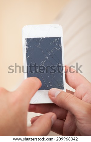 Cropped image of man\'s hand holding smartphone with broken screen at home