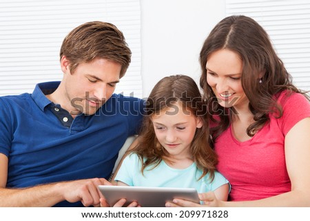 Family of three using digital tablet together while relaxing on sofa at home