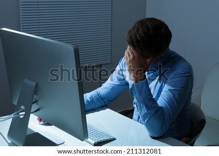 Overstressed businessman leaning at computer desk in office