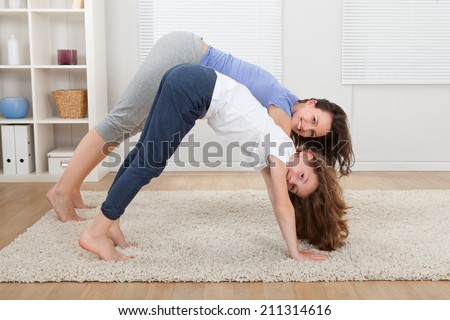 full length portrait of smiling mother and daughter performing yoga in downward facing dog pose at home