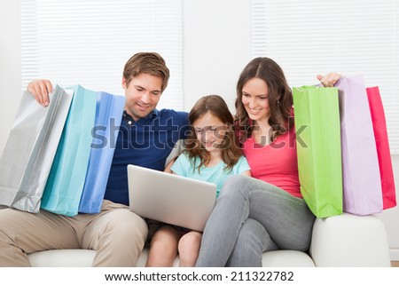 Happy family with shopping bags using laptop while relaxing on sofa at home