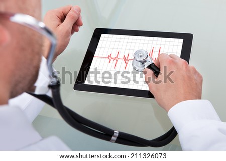Cropped image of male doctor analyzing heartbeat on digital tablet through stethoscope