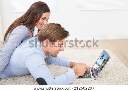 Side view of couple looking at photos on laptop while lying on rug at home