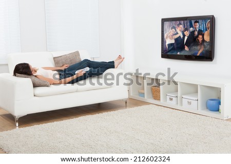 Full length of young woman watching television while lying on sofa at home