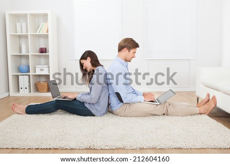 Full length of couple using laptops while sitting on rug in living room