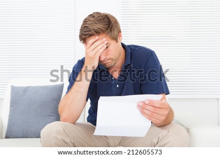 Stressed mid adult man holding bill while sitting on sofa at home