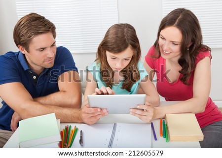 Parents assisting daughter in using digital tablet while studying at home