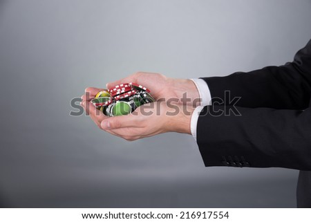 Cropped image of businessman\'s hands holding poker chips in cupped hands against gray background