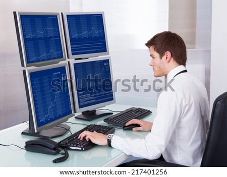 Portrait Of Young Stock Broker Using Computer At Desk