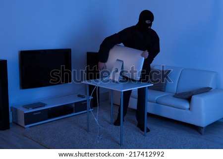Full length of thief stealing computer monitor from living room