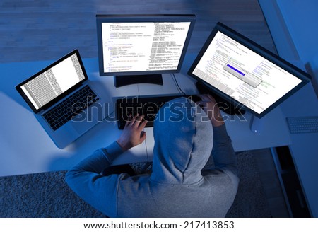 Side view of hacker using multiple computers to steal data at table