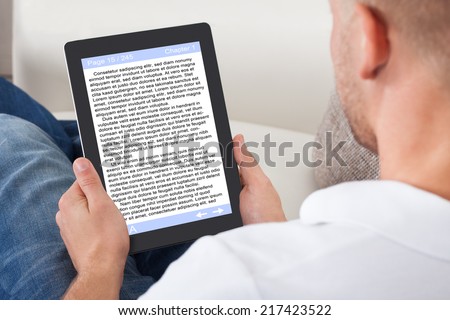 Man relaxing at home reading an e-book online or studying long distance on his tablet