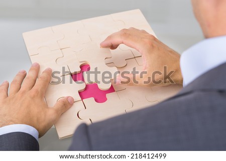 Businessman assembling jigsaw puzzle. Over the shoulder view