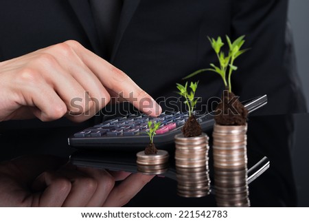 Midsection of businessman using calculator by stacked coins with plants on desk