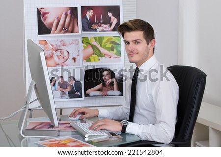 Side view young male photo editor using laptop at desk in office