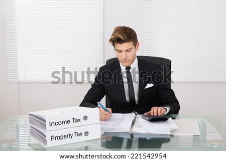 Young businessman calculating tax with binders at desk in office