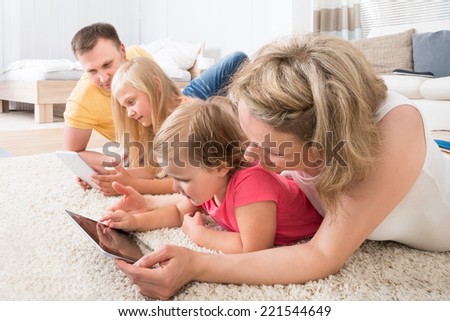 Family Using Tablets Lying On Carpet At Home