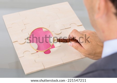 Businessman inspecting jigsaw puzzle. Over the shoulder view