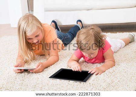 Kids Using Tablet Lying On Carpet At Home