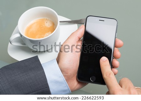 Berlin; Germany - October 10; 2014: Photo of businessman holding Apple iPhone 6 at table. Apple iPhone 6 was launched on September 19; 2014