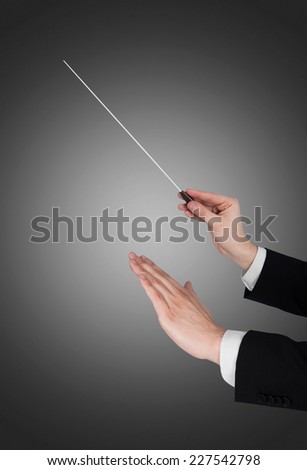 Cropped image of music conductor\'s hands holding baton against gray background
