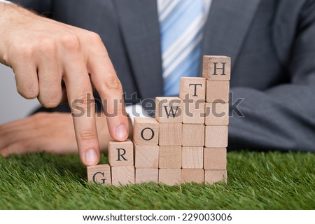 Midsection of businessman climbing growth blocks with fingers on grass
