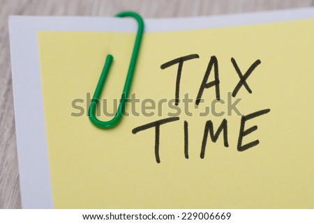 Closeup of Tax Time written on yellow paper note with paperclip