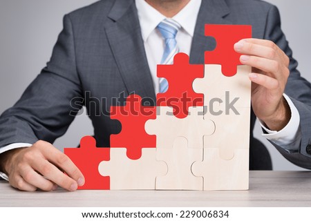 Midsection of businessman holding red jigsaw graph on table against gray background