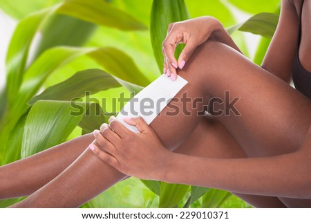 Low section of African American woman waxing leg against leaves