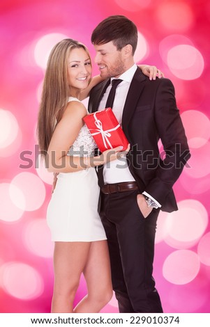 Portrait of happy woman holding gift while embracing boyfriend against pink background