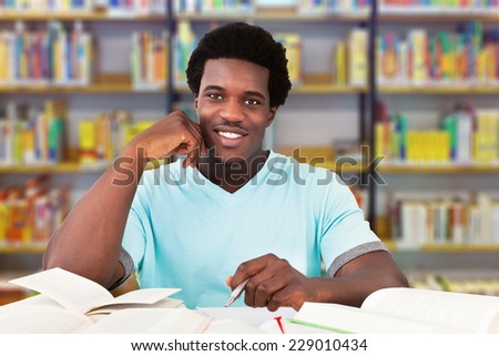 Portrait of smiling male university student studying at table in library
