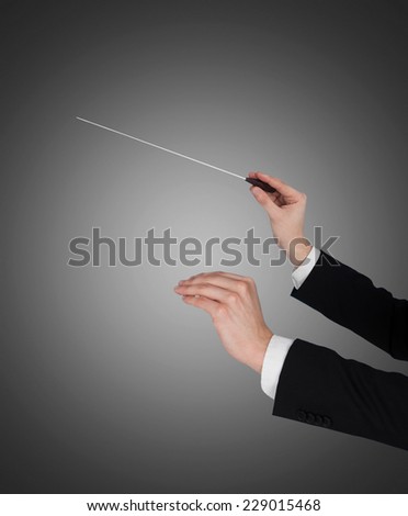 Closeup of music conductor\'s hands holding baton against gray background